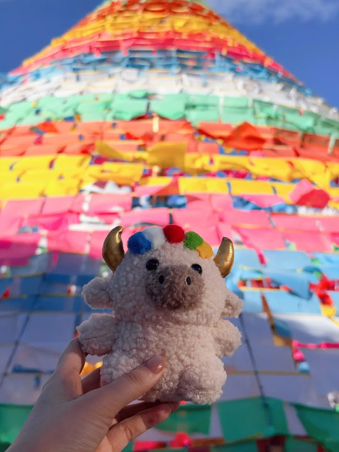 Close-up of Dele held up in front of a towering cone of colourful prayer flags — 經幡塔前的德勒特寫