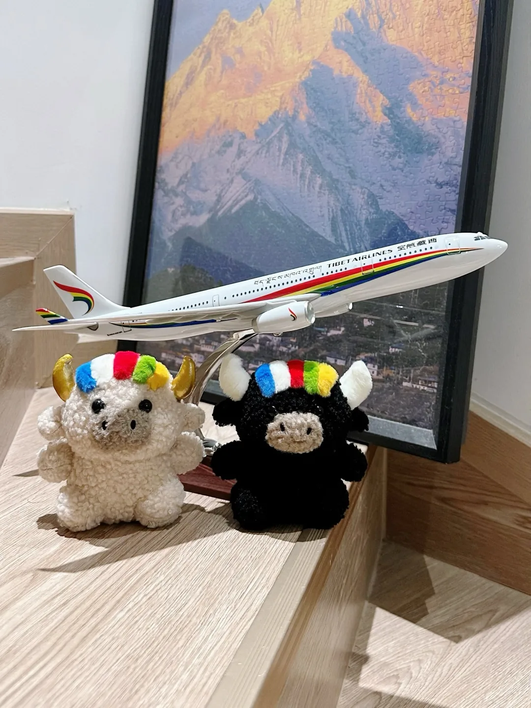 Tashi and Dele in front of a Tibet Airlines model plane and a golden snow-mountain puzzle — 西藏航空飛機模型與雪山拼圖前的扎西與德勒