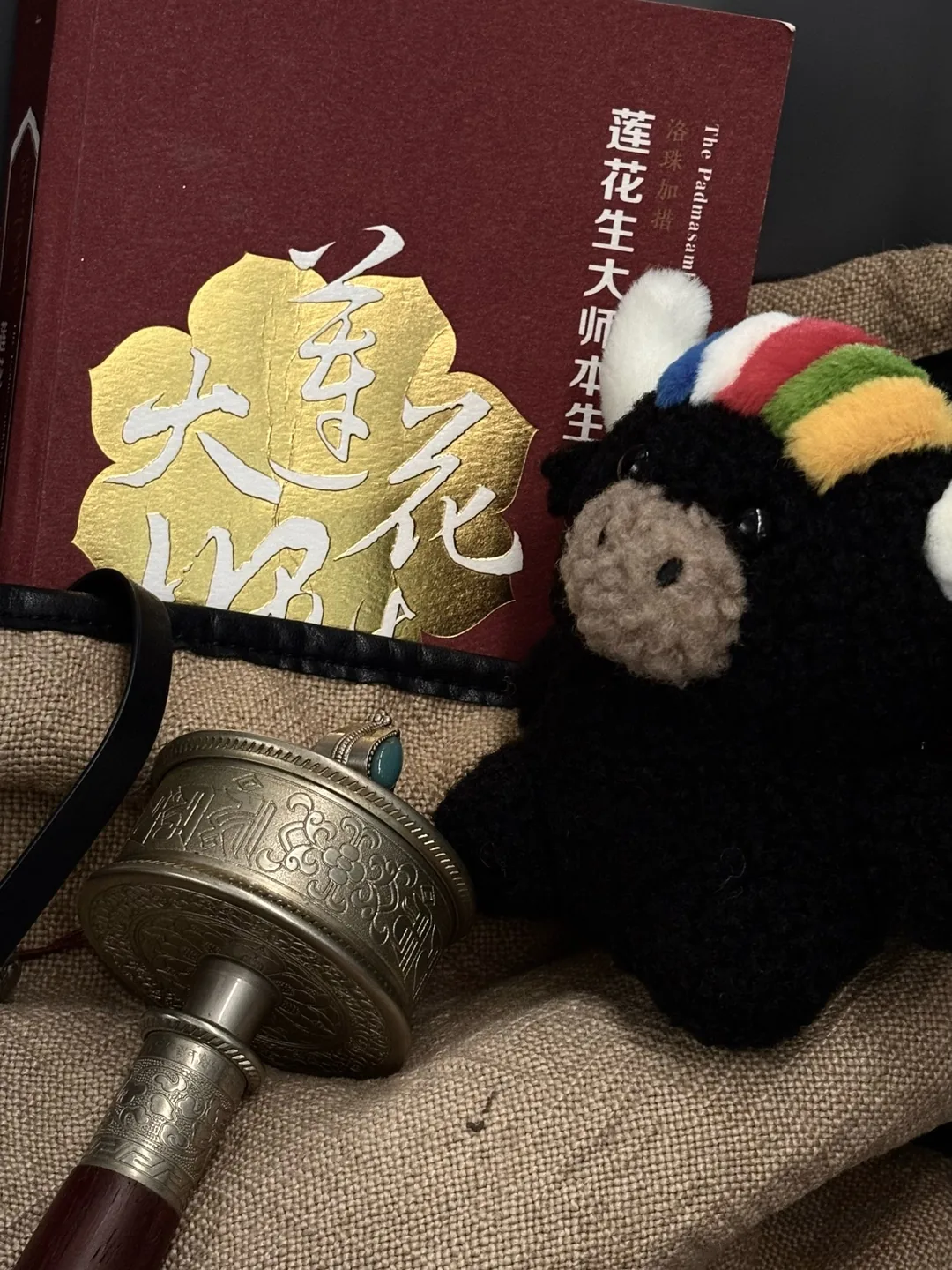 Tashi beside a book on Padmasambhava and a carved prayer wheel — 扎西陪著《蓮花生大師本生傳》與轉經筒